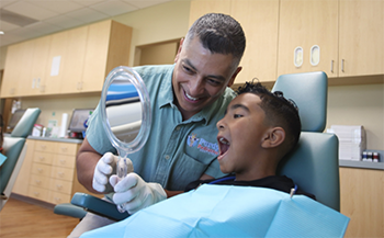 Young boy shaking hands with his dentist while his mother holds him